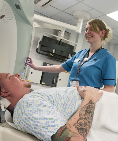 A smiling nurse with a patient lying down about to go inside a medical body scanner