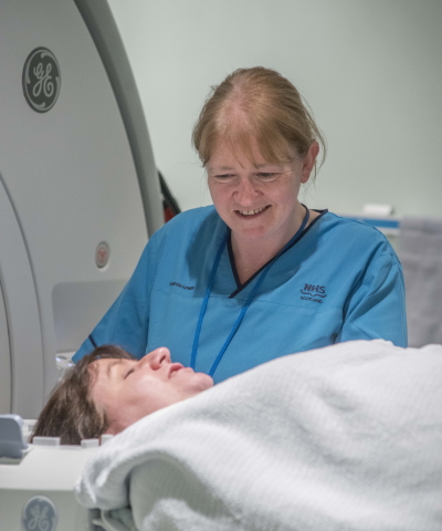 A smiling nurse with a patient lying down about to go inside a medical body scanner